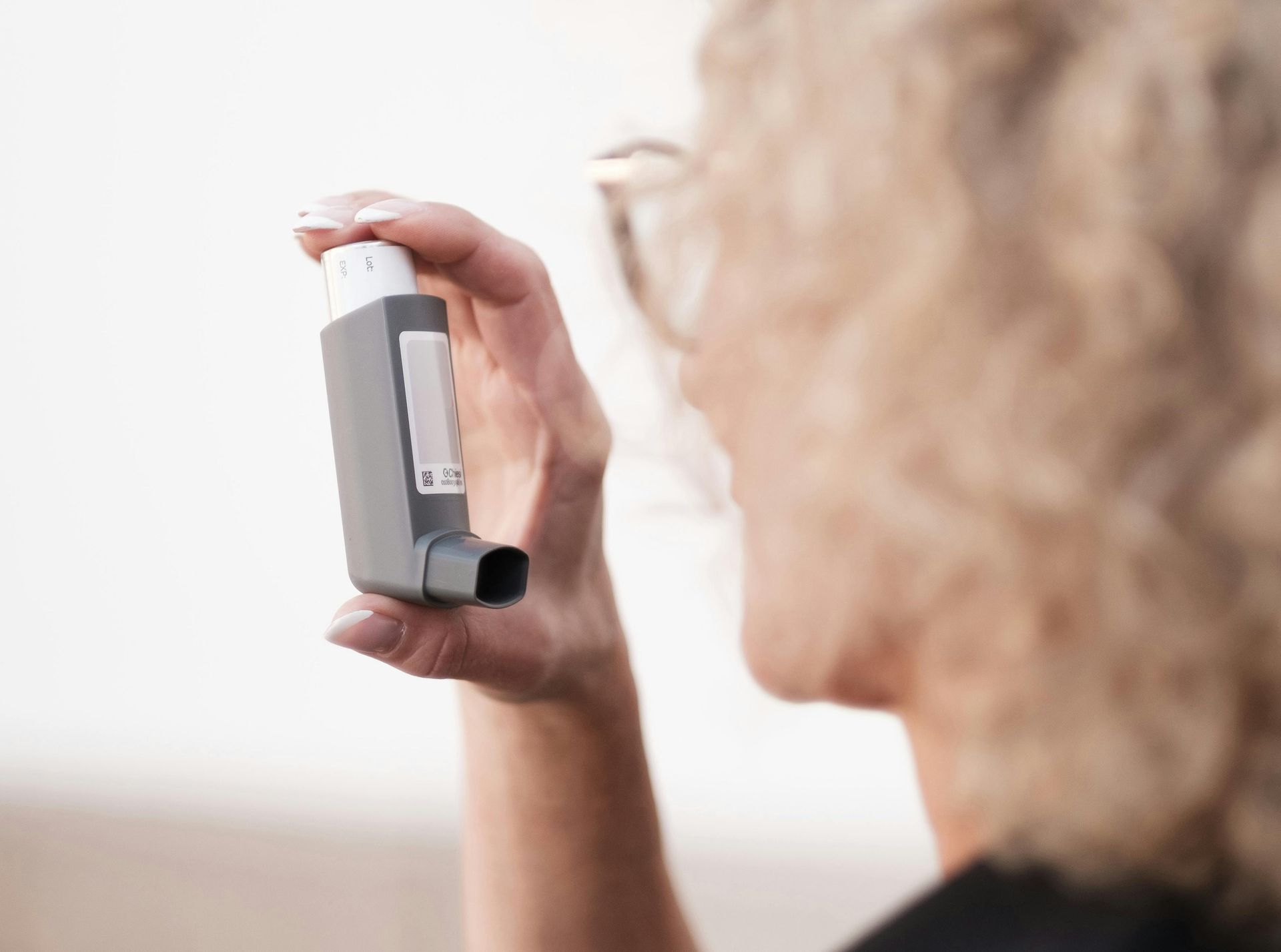 A person with curly hair holds a gray asthma inhaler near their mouth, preparing to use it, while considering complementary options like acupuncture for asthma.